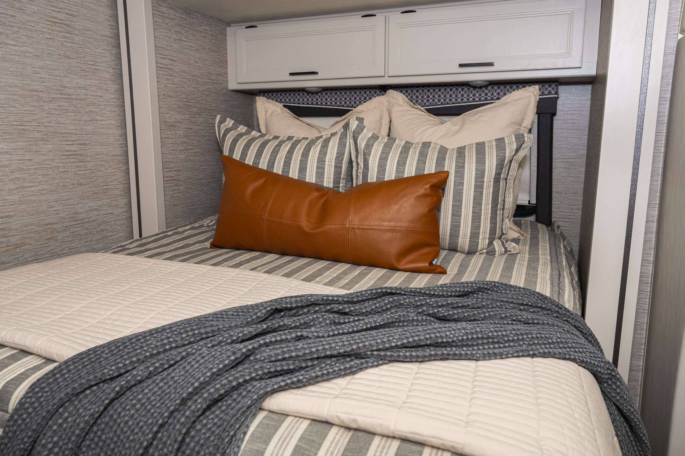 A bed made in an RV with classic stripe and calming neutrals zipper bedding with tan, gray and rustic accessories.
