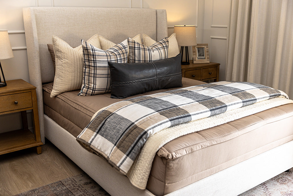 A bed made with tan zipper bedding and an assortment of neutral plaid pattern pillows and blanket.