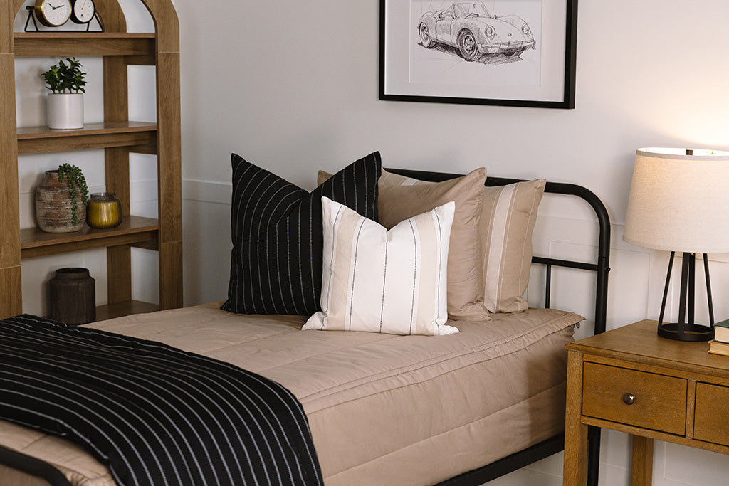 A twin bed made with tan zipper bedding an adorned with neutrals pillows and a matching striped blanket.