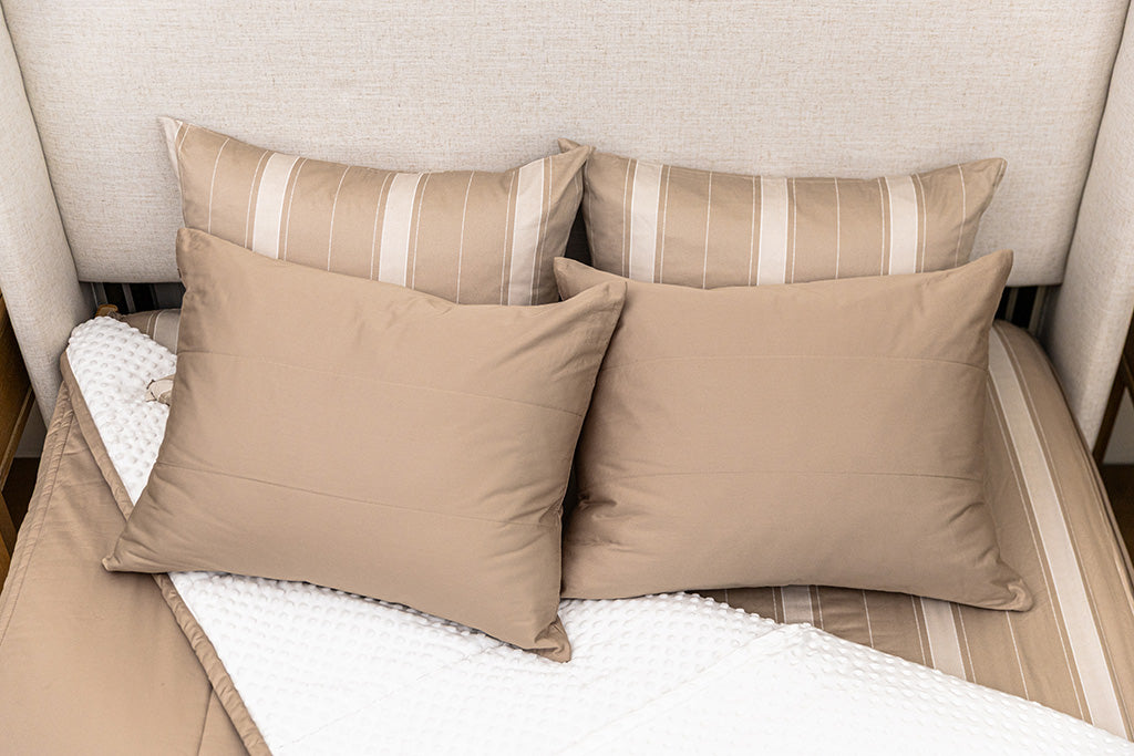 A bed made with tan zipper bedding with the comforter pulled back and pillows on top of the bed.