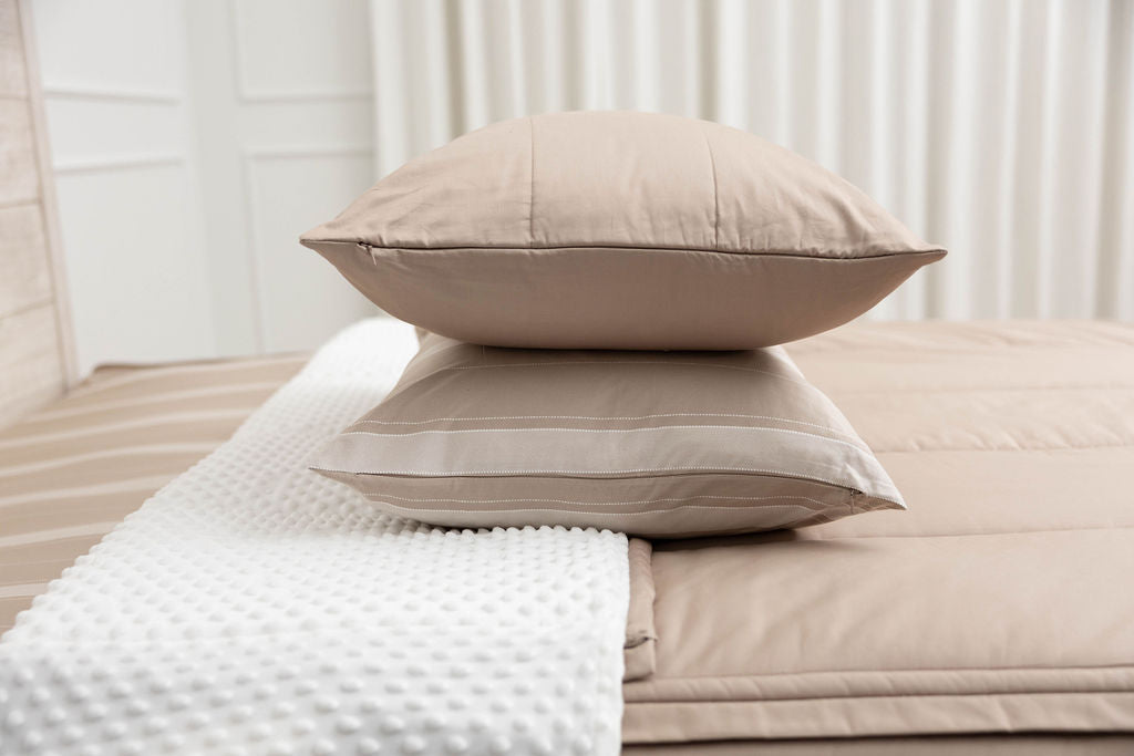 A tan striped pillowcase and matching sham on a made bed with tan zipper bedding. 
