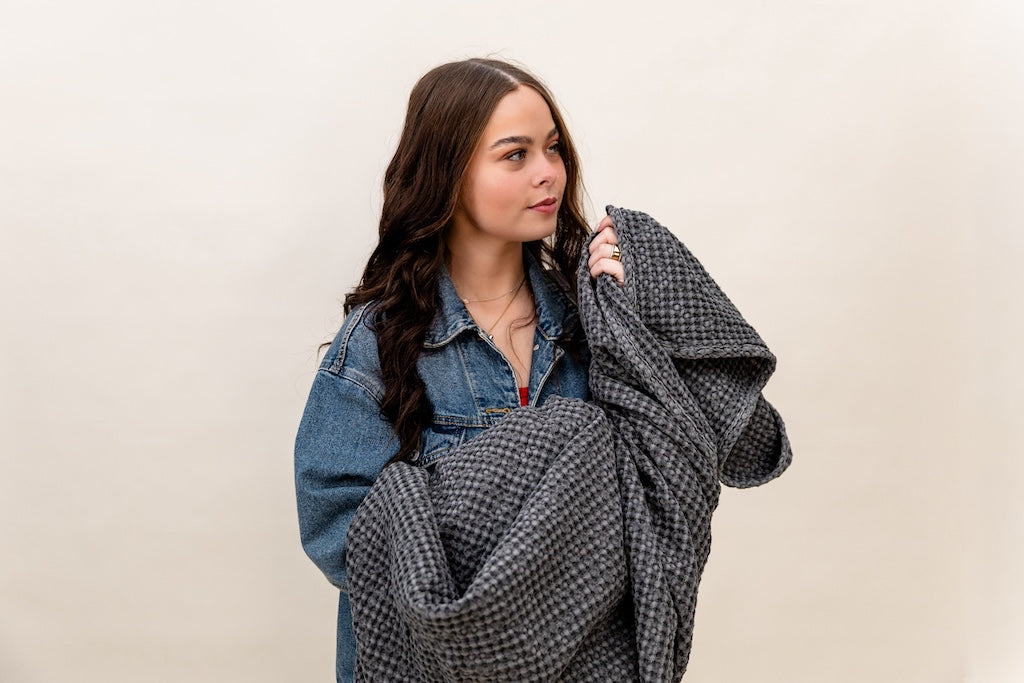 Girl holding a  gray textured waffle weave blanket on a tan background.