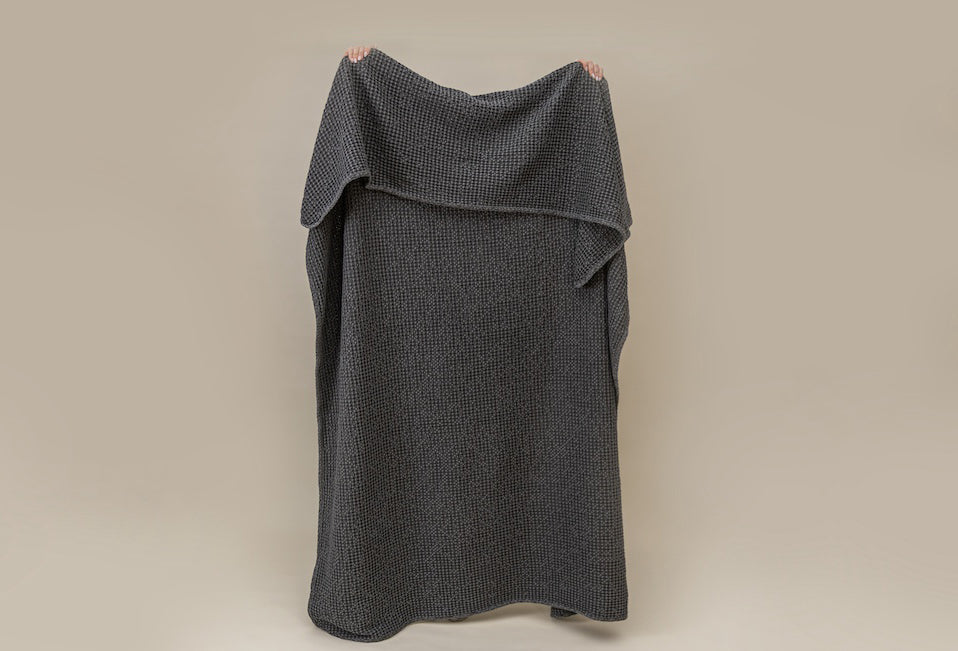 A person holding a  gray textured waffle weave blanket on a tan background.