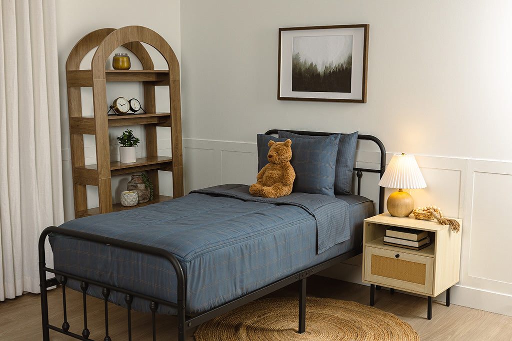 Zipper bedding in a bedroom on a black, twin bed frame that has a slate blue grid print, with a stuffed toy laying against the pillow.