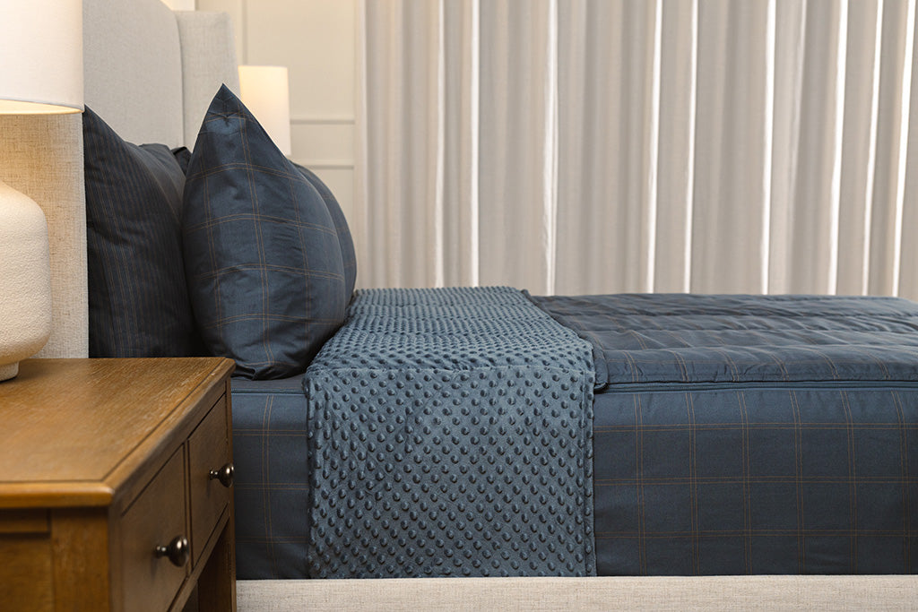 A bed made with slate blue grid printed zipper bedding, showcasing the pillowcase and sham and the top of the bedding turned down to show the inside lining. 