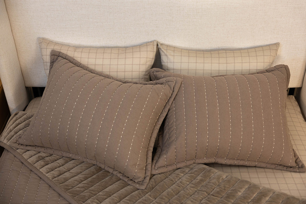 a bed made with brown zipper bedding, the top pulled back to reveal the inside lining and four pillows thrown on top