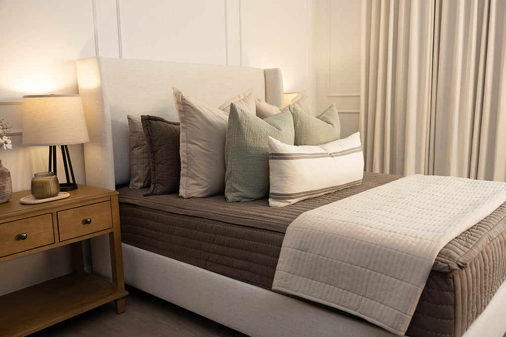 A queen bed made with brown zipper bedding and an assortment of cream and sage bedding accessories