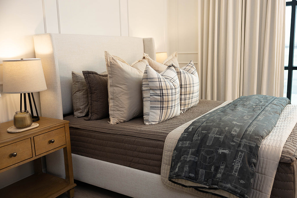 a bed made with brown zipper bedding and an assortment of neutral and plaid bedding accessories