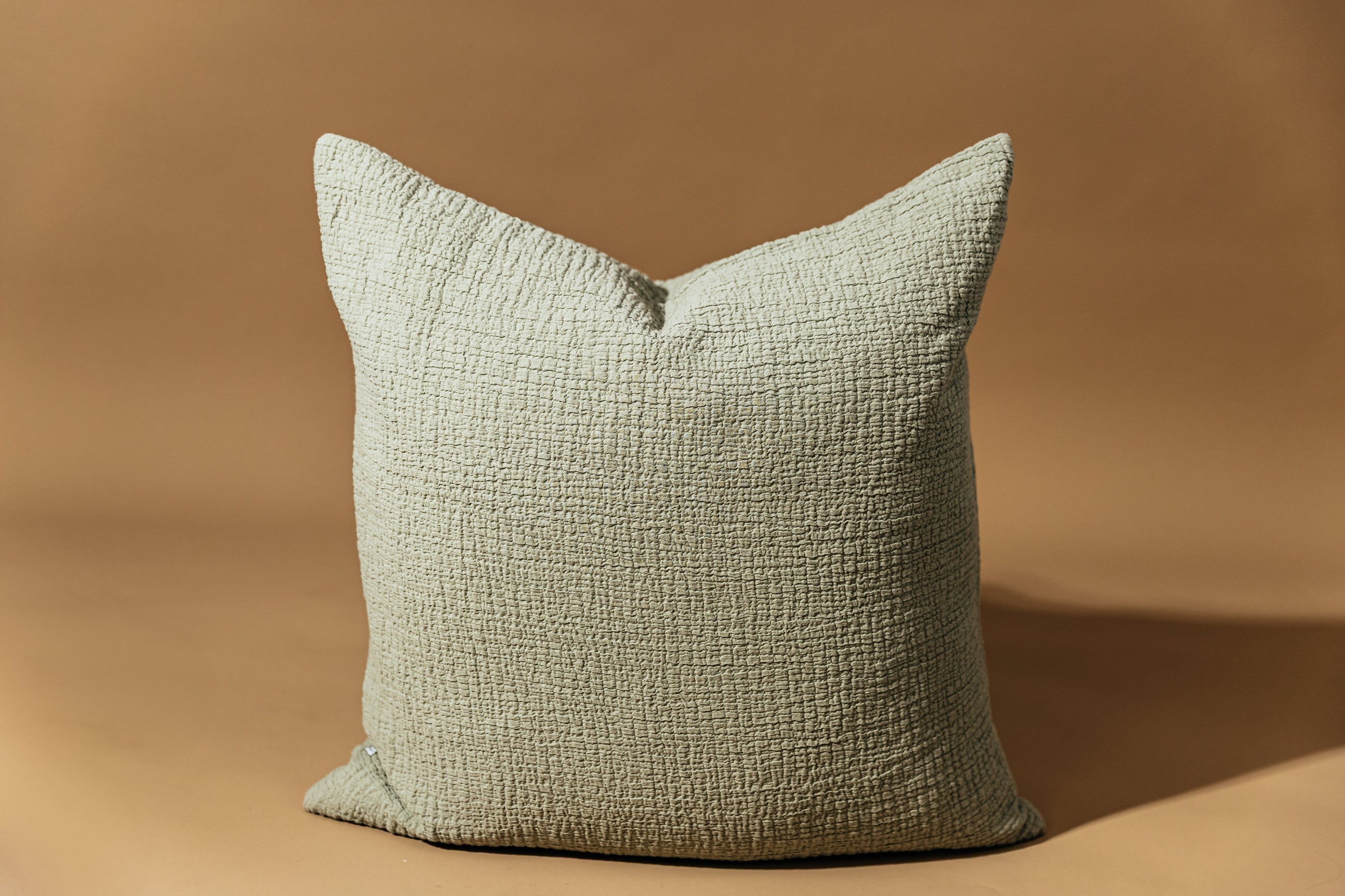A sage green crinckle textured euro pillow arranged on a brown background.