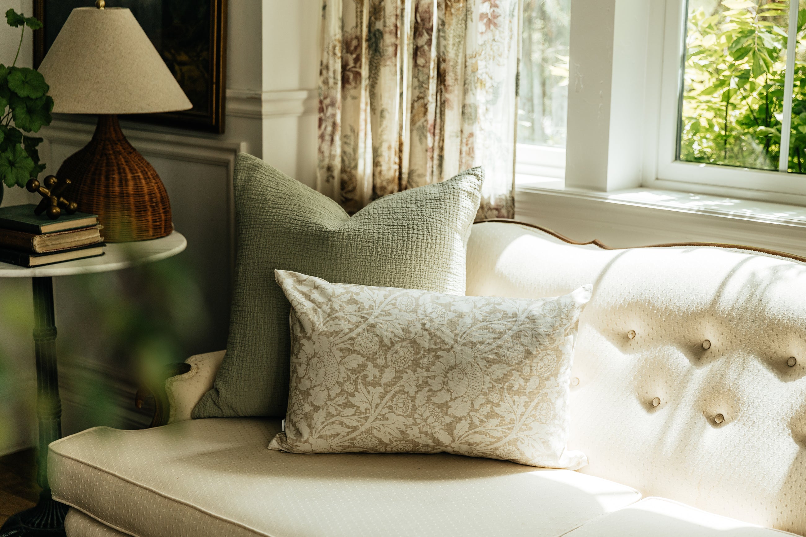 A sage green and floral pillow arranged on a cream textured antique couch.