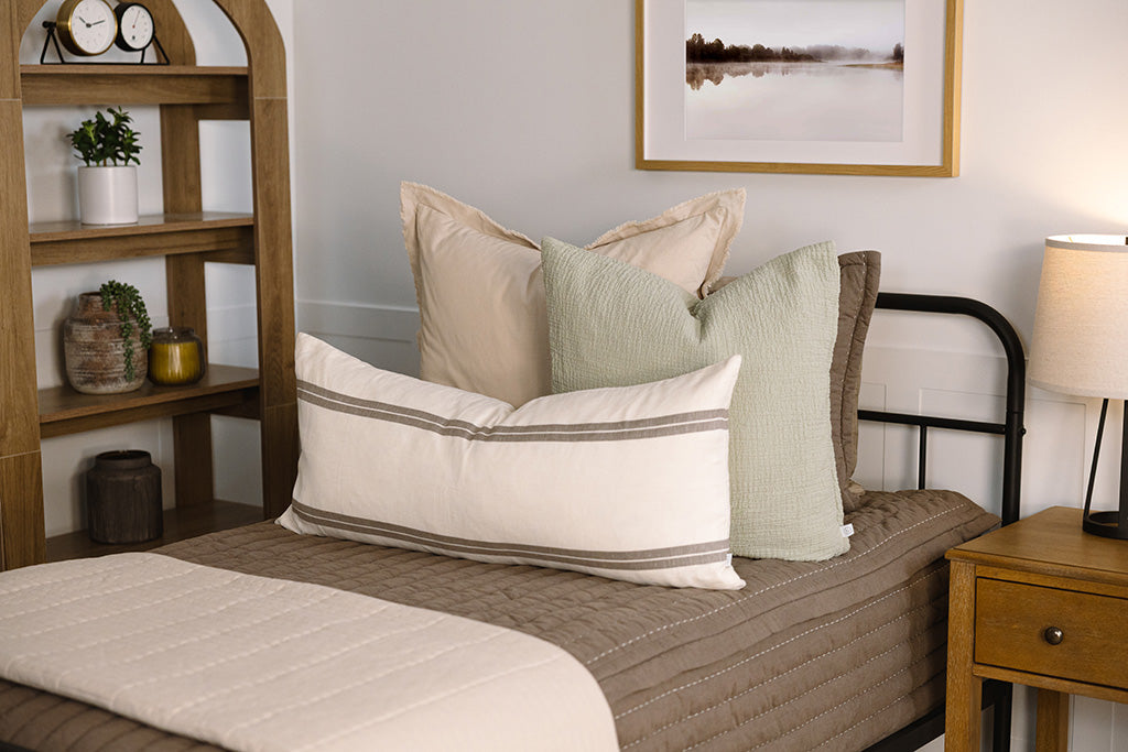 A twin bed made with brown zipper bedding and an assortment of neutral and sage bedding accessorie