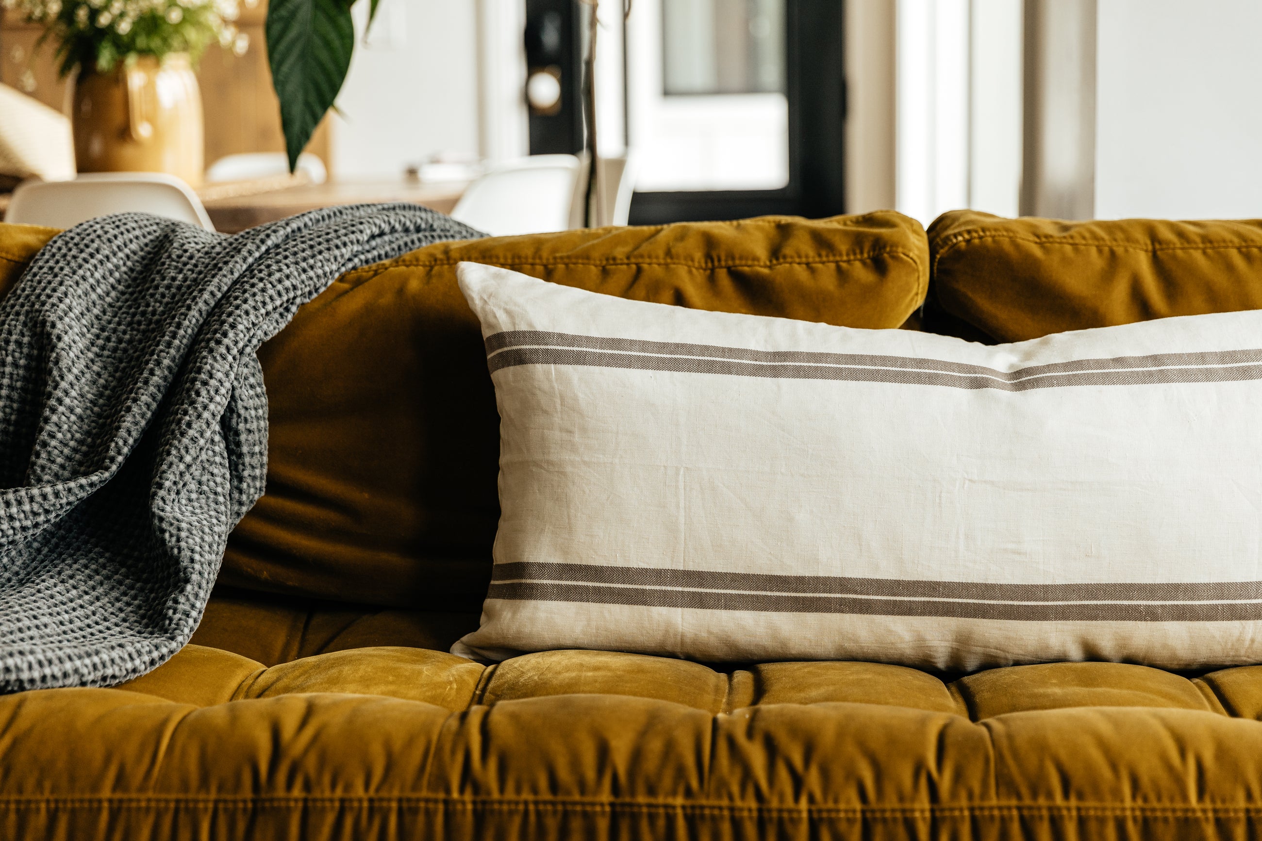 An XL cream lumbar pillow with brown stripes and arranged on a couch with a blanket.