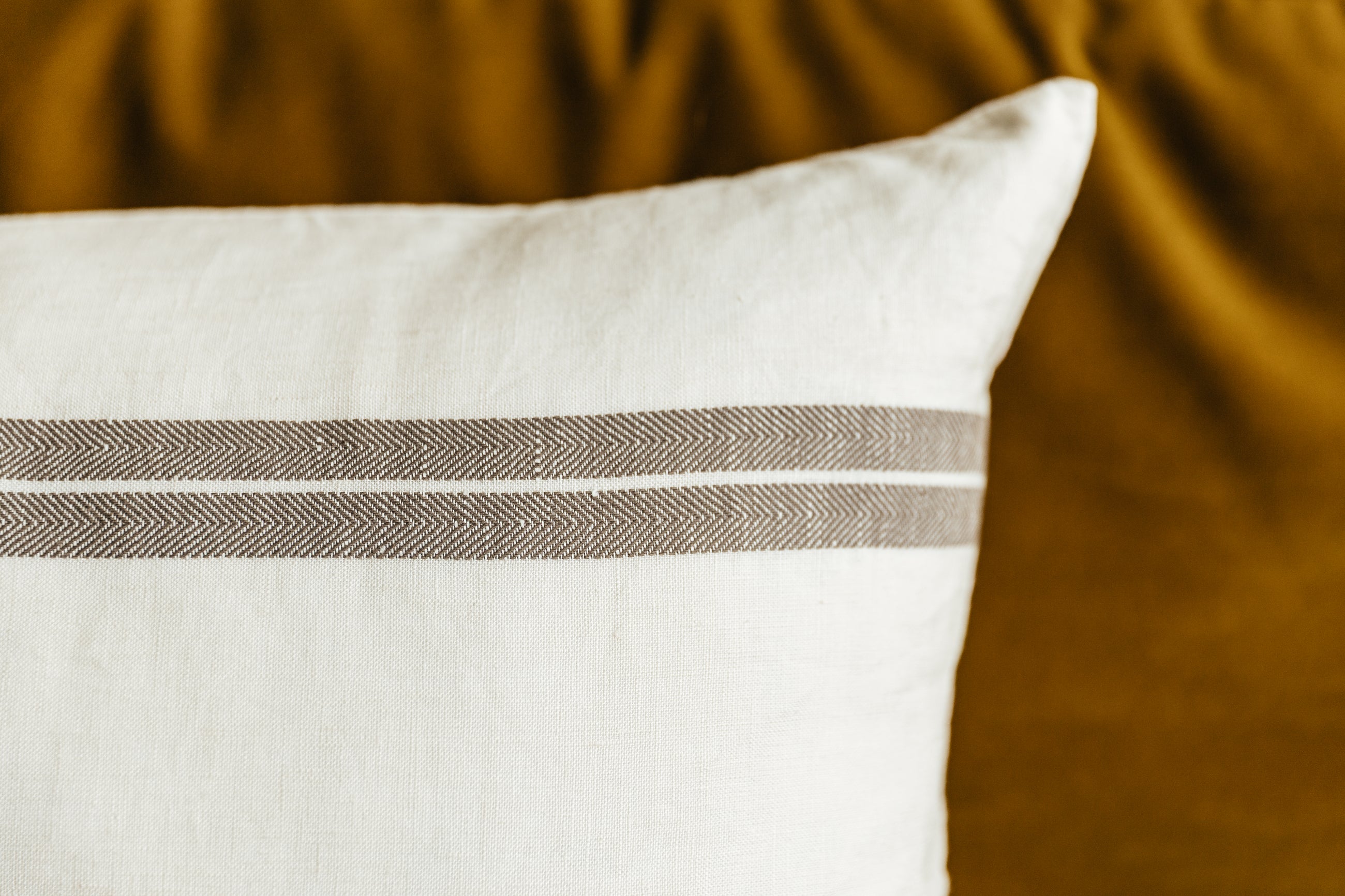 A close up view of an XL cream lumbar pillow with brown stripes.