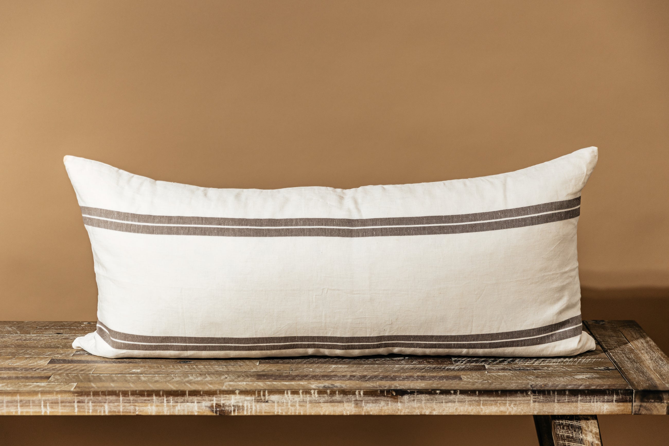 An XL cream lumbar pillow with brown stripes and arranged on a bench.
