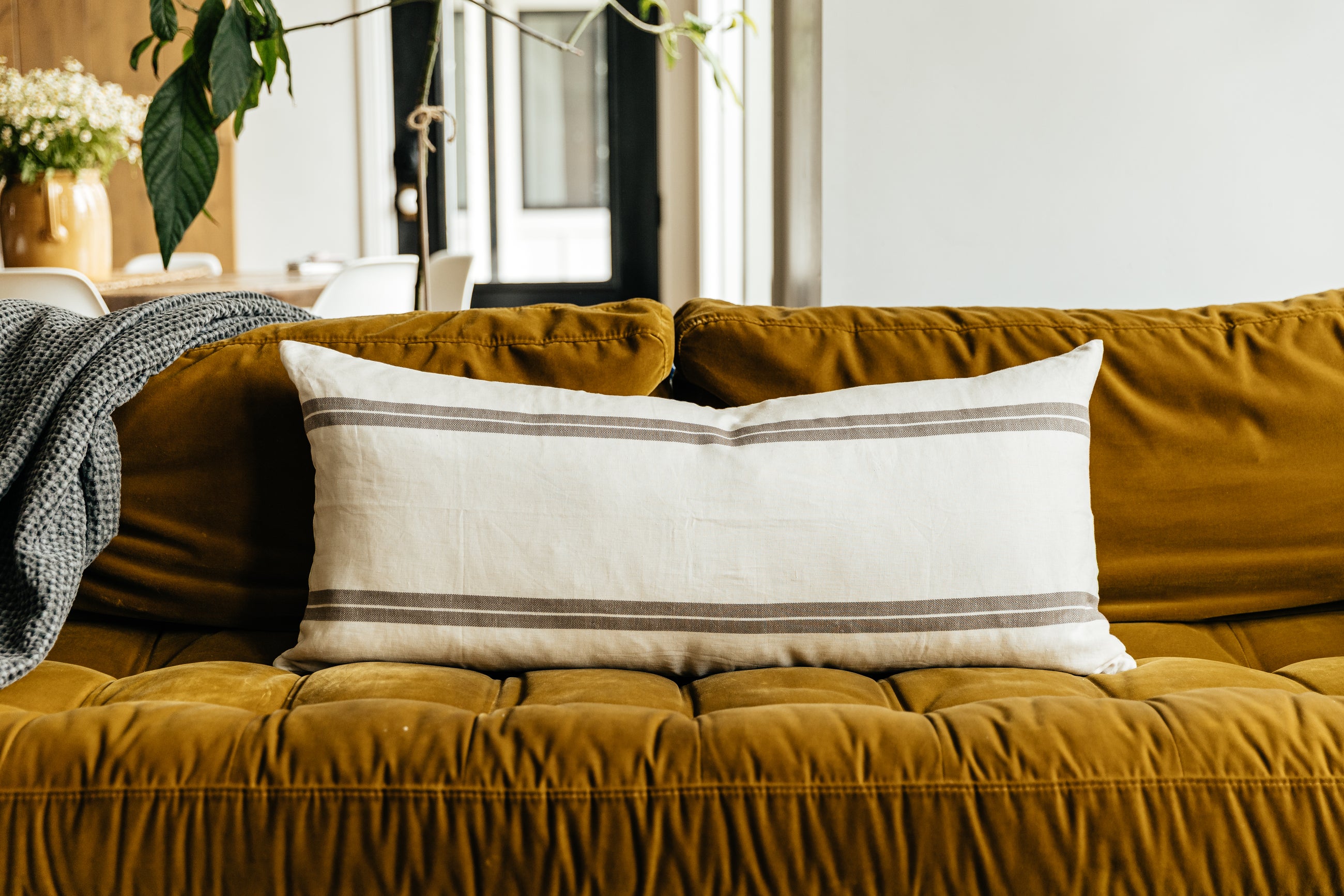 An XL cream lumbar pillow with brown stripes and arranged on a couch.