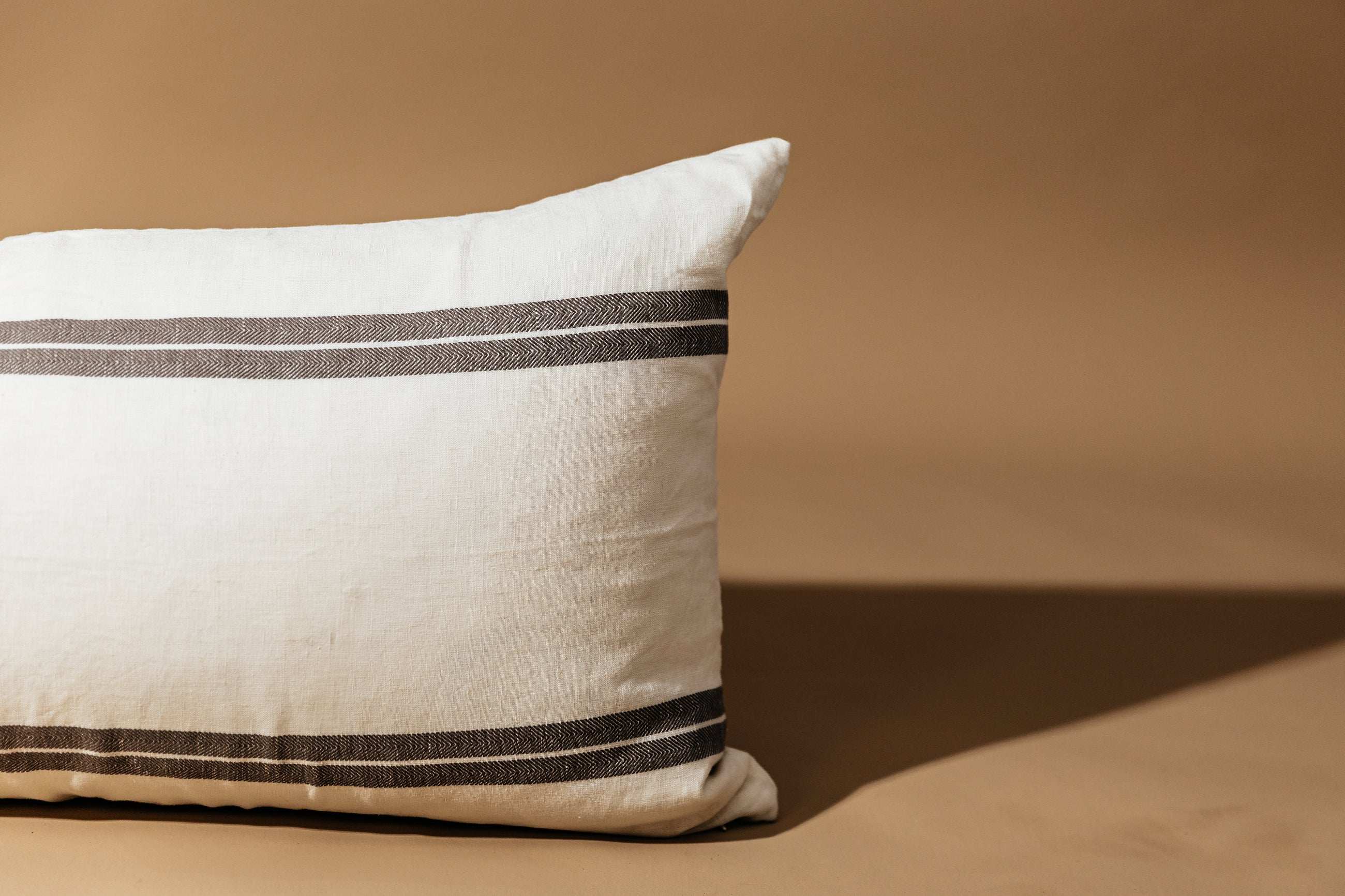 A close up view of an XL cream lumbar pillow with brown stripes arranged on a brown background.