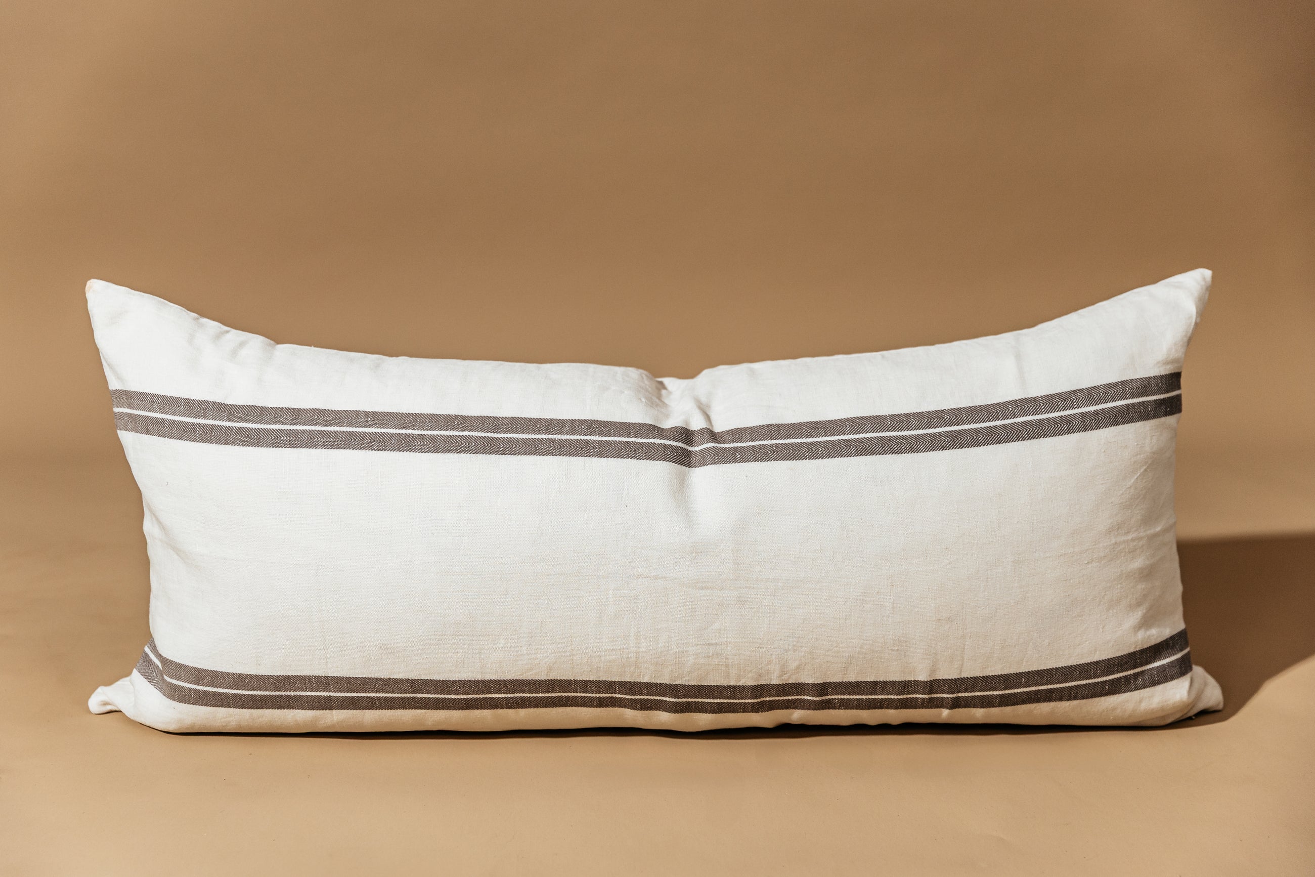An XL cream lumbar pillow with brown stripes and arranged on a brown background.