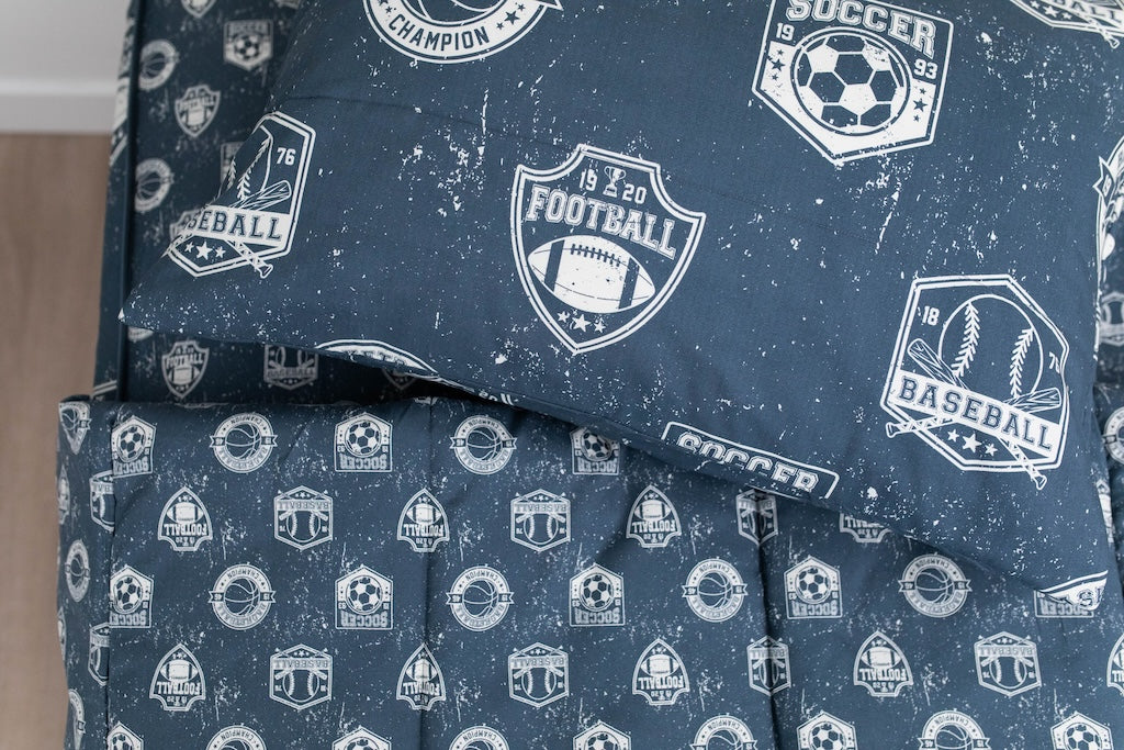 A twin bed made with blue sports themed kids zipper bedding with the top unzipped and pulled back and a pillow on top