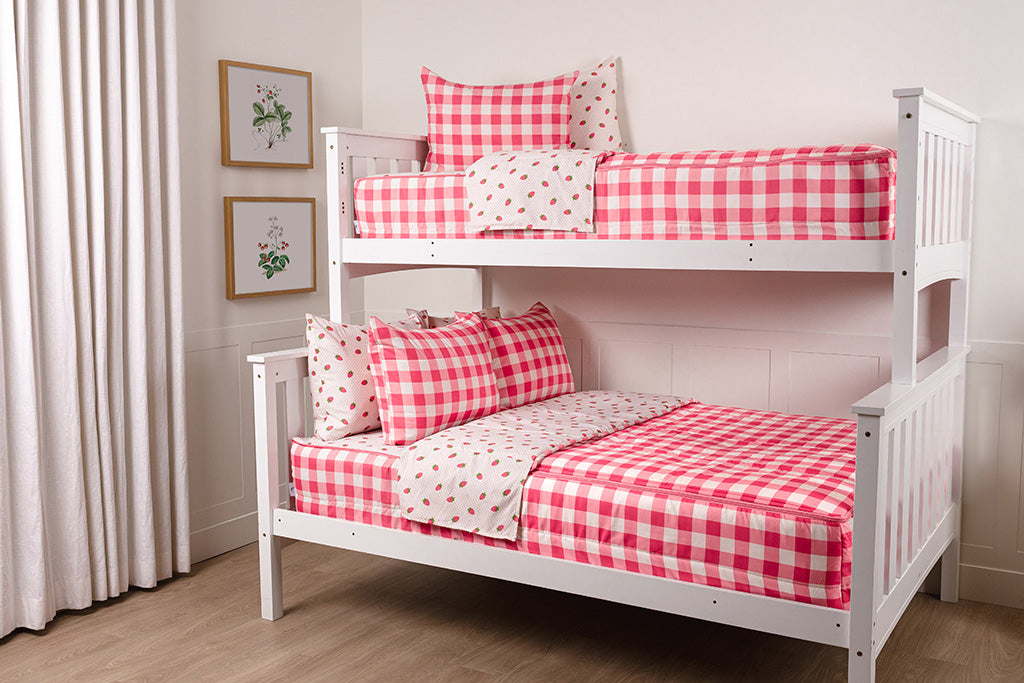 A bunk bed with the top twin and bottom full made with pink gingham and strawberry printed zipper bedding.