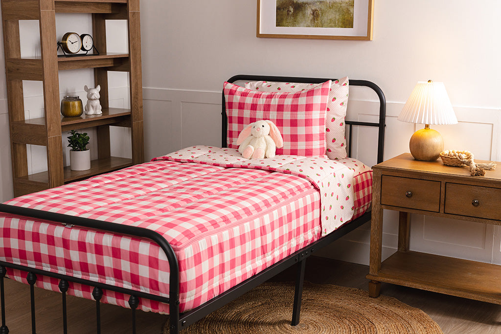 Children's zipper bedding in a bedroom on a black bed frame that has a pink gingham exterior and strawberry print interior, with a stuffed toy laying against the pillow.