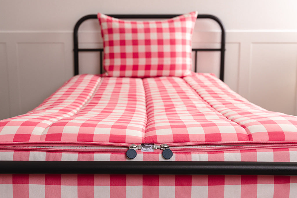 A shot of the two zippers on a set of pink gingham zipper bedding, the zippers completely unzipped to show how they meet at the foot of the bed. 