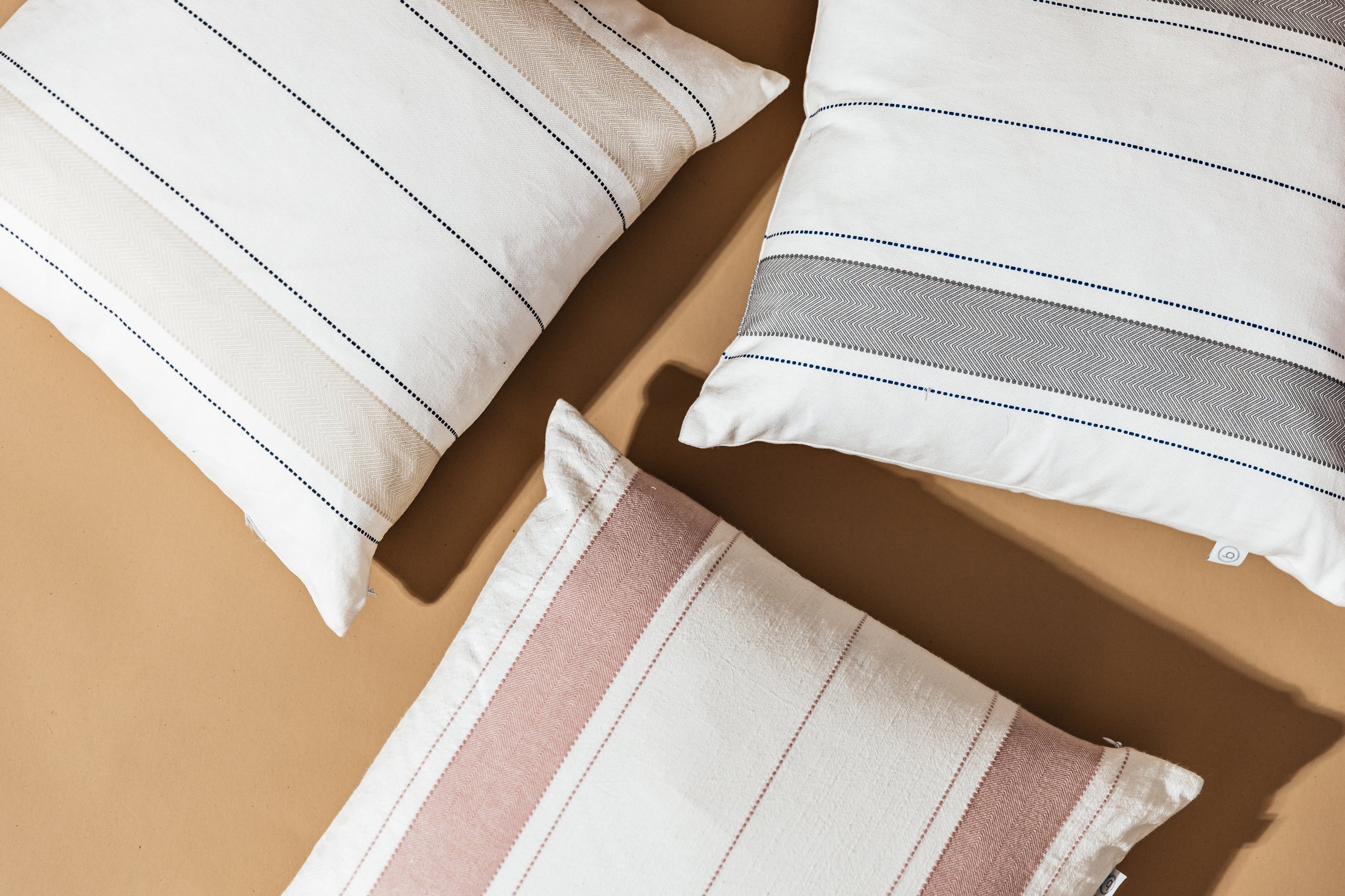 3 striped pillow with similar striped design in varying colors sitting on a brown backdrop.
