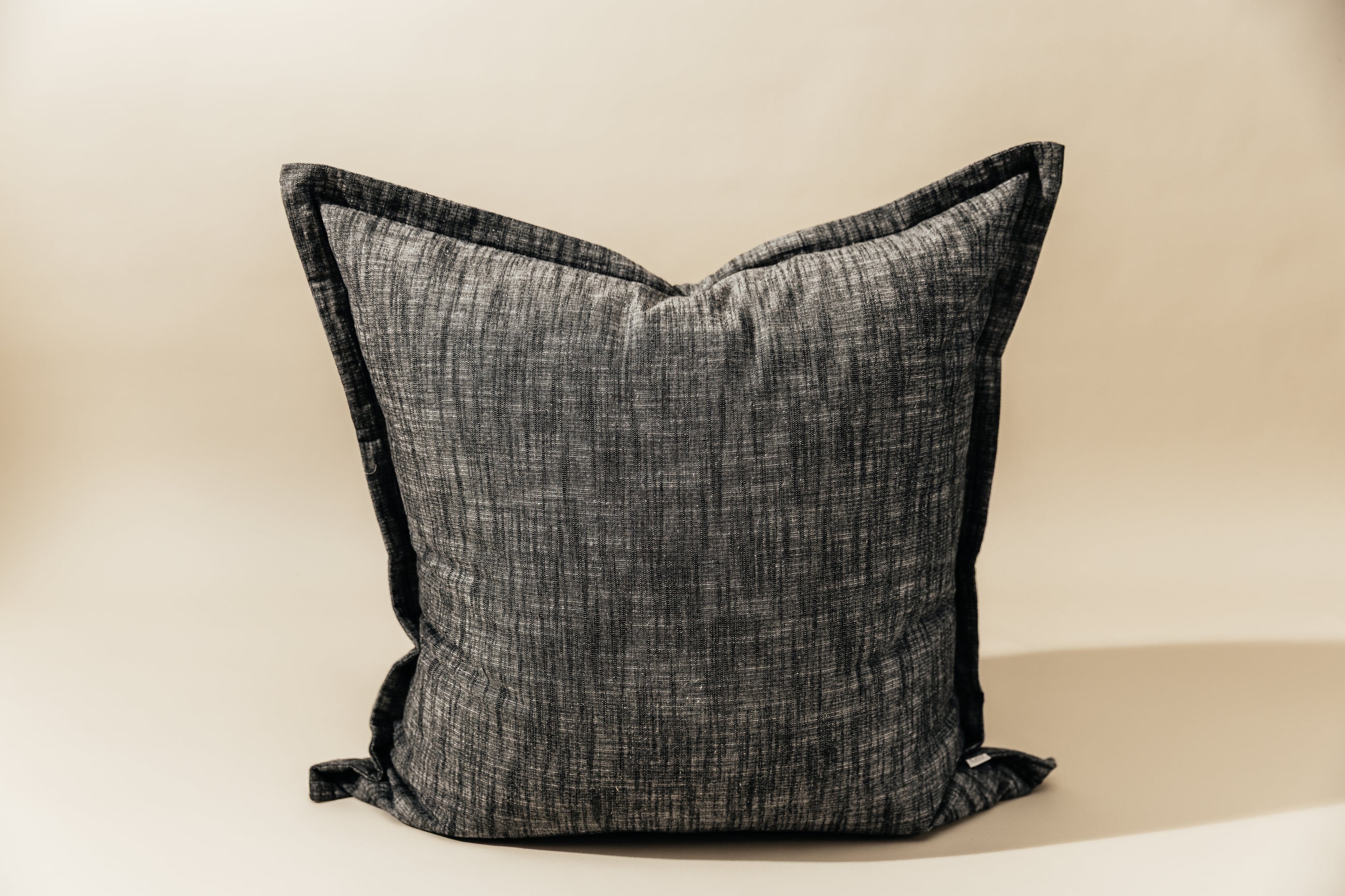 A large charcoal gray pillow on a cream background.
