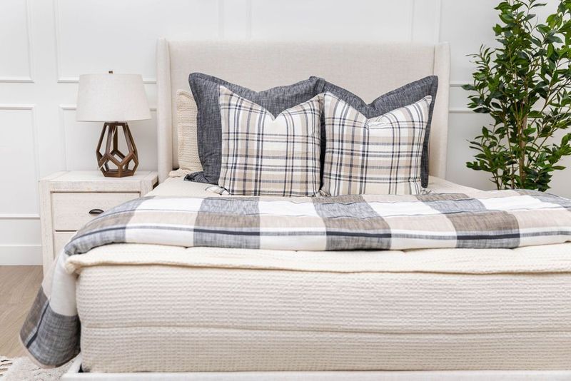 A queen bed made with cream waffle textured zipper bedding and neutral and plaid pattern pillows and blanket.