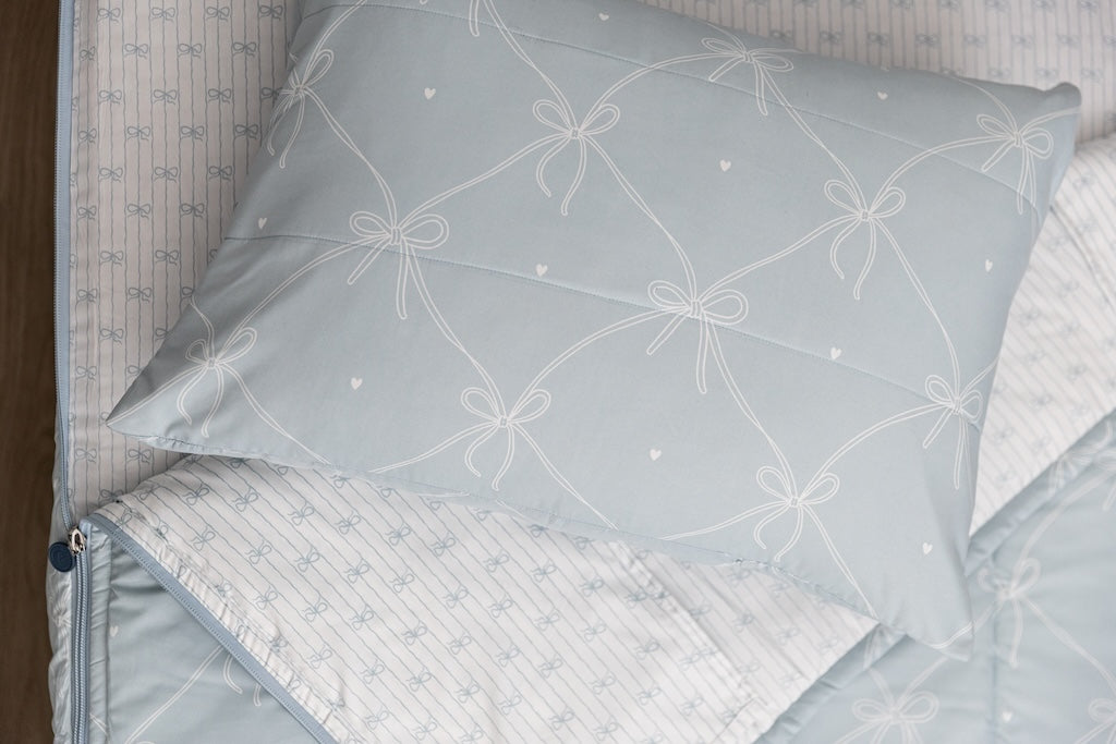 Bows printed kids zipper bedding with the top unzipped and one side pulled back to reveal the inside lining, the pillow tossed on top of the bed.