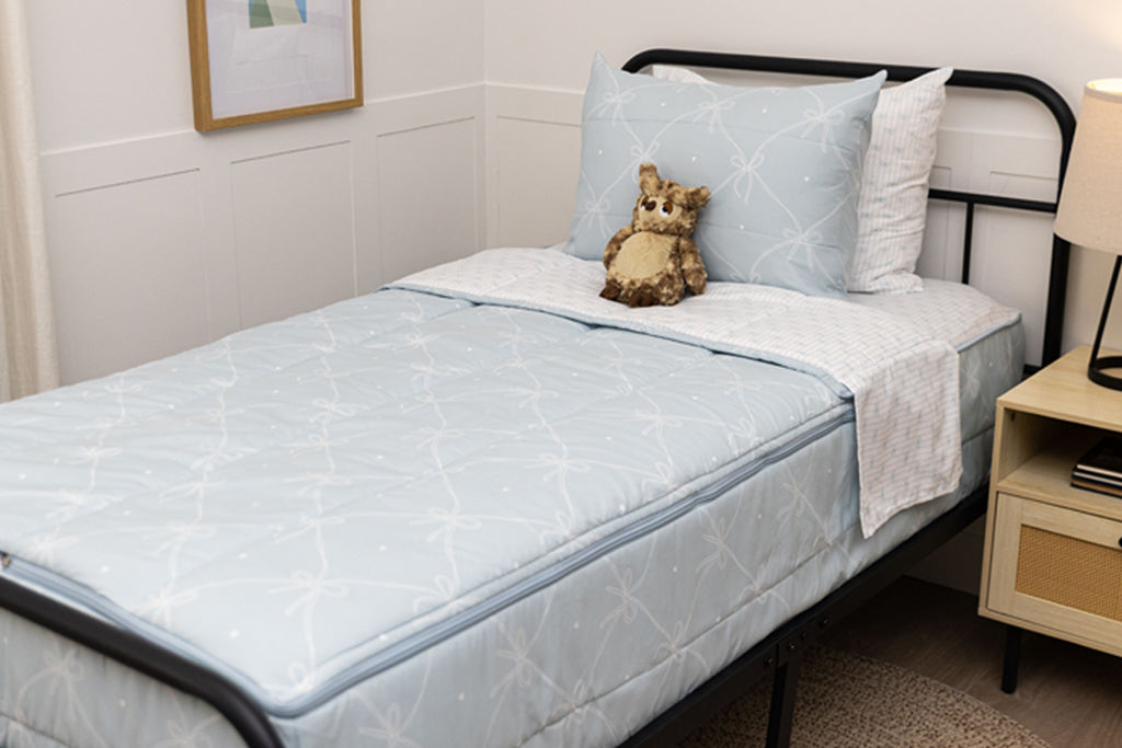 A twin bed made with bows zipper bedding, a nightstand beside the bed and a stuffed animal propped up against the pillow.