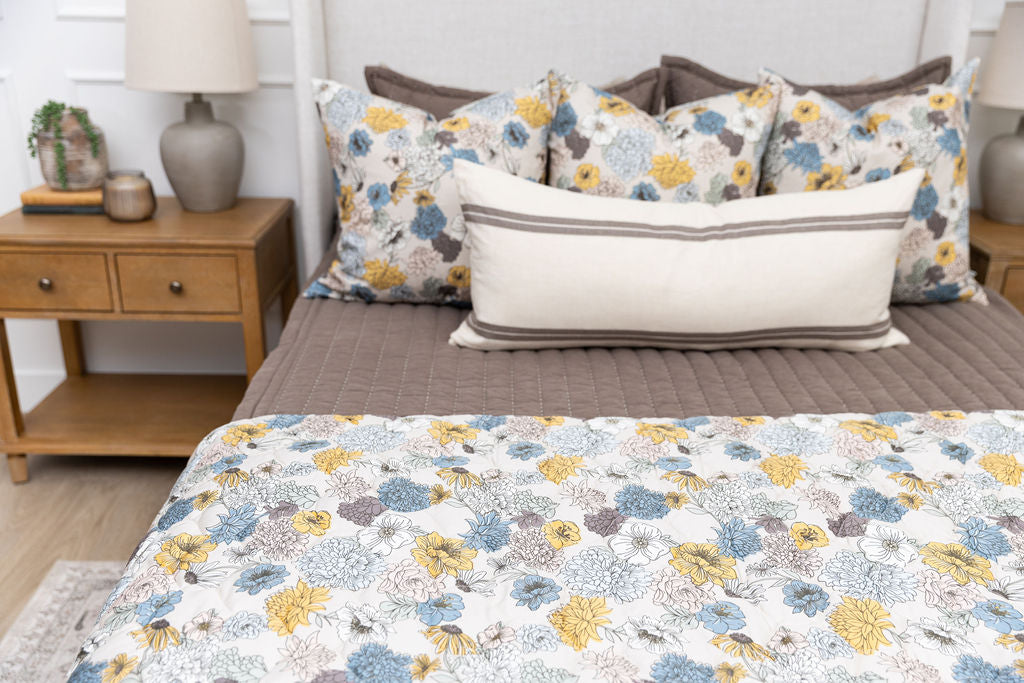 A queen bed made with brown zipper bedding and blue and yellow floral bedding accessories