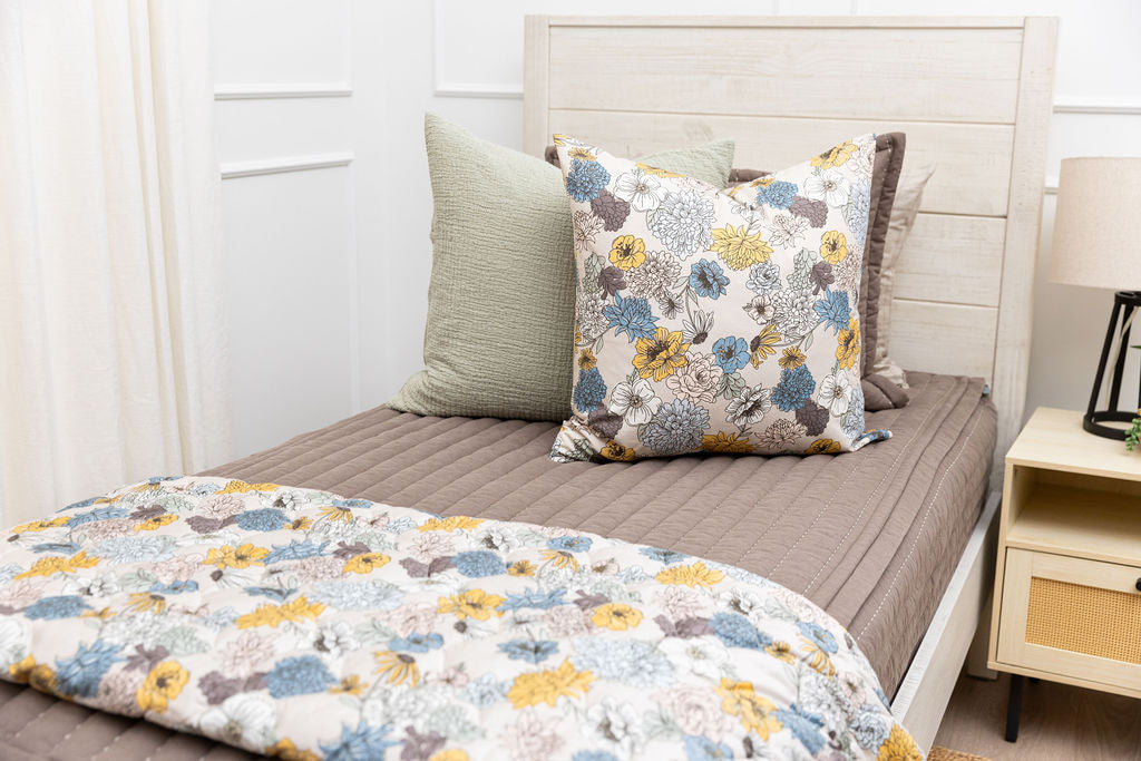 A twin bed made with brown zipper bedding and blue and yellow floral bedding accessories
