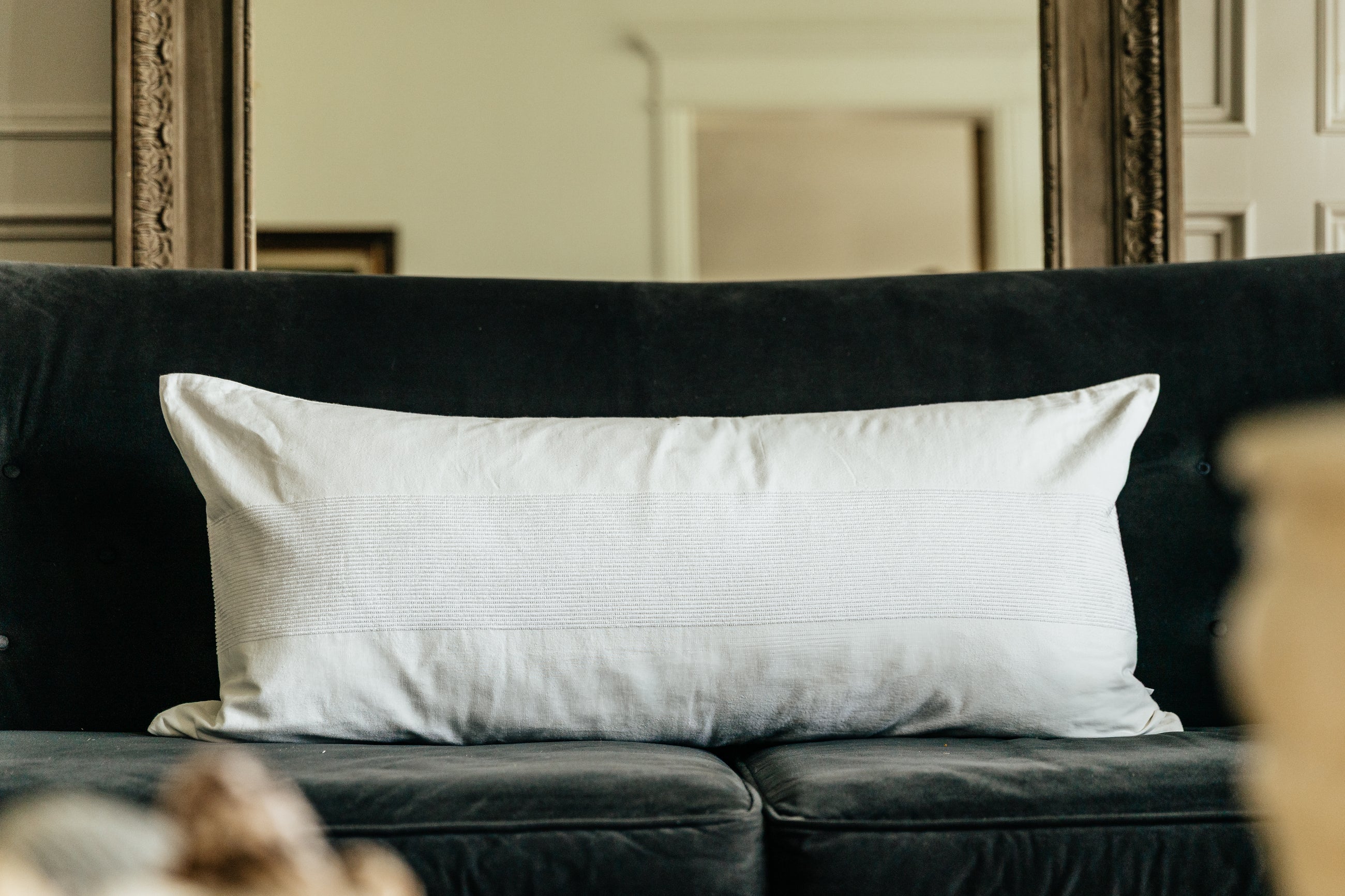 A white lumbar pillow on a black velvet couch.