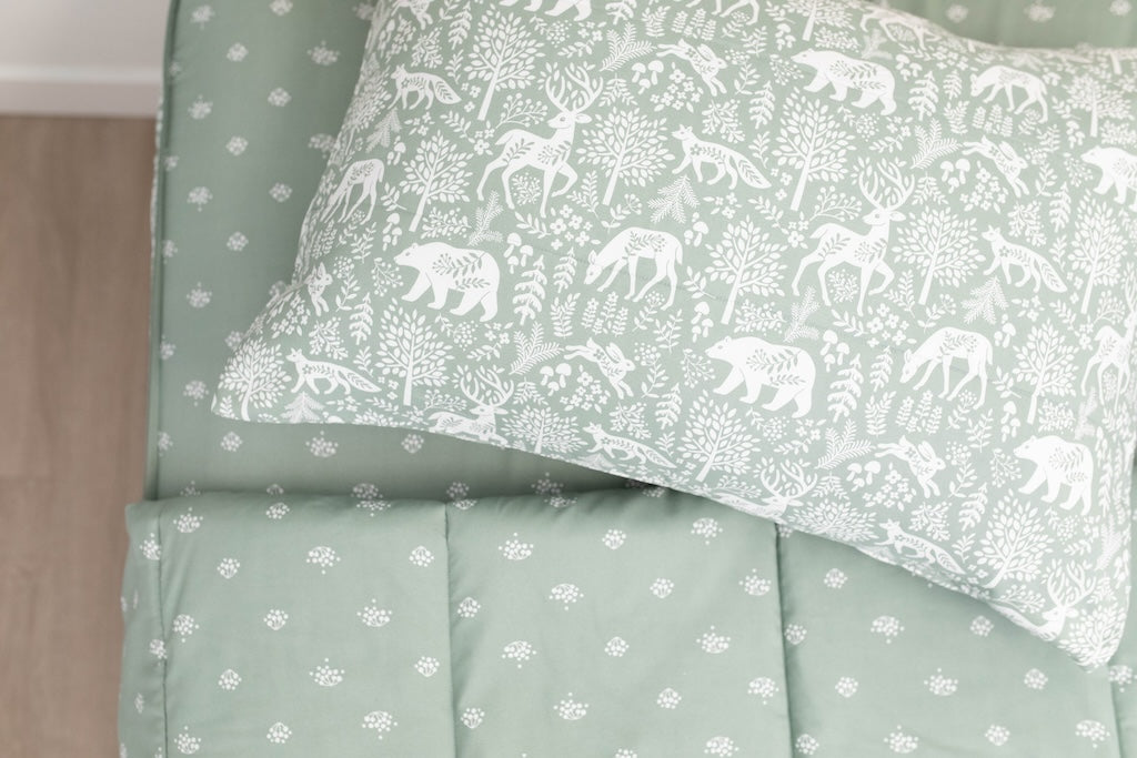 A twin bed made with sage green woodland creatures and trees kids zipper bedding, the top unzipped and slightly pulled back and a pillow on the bed.