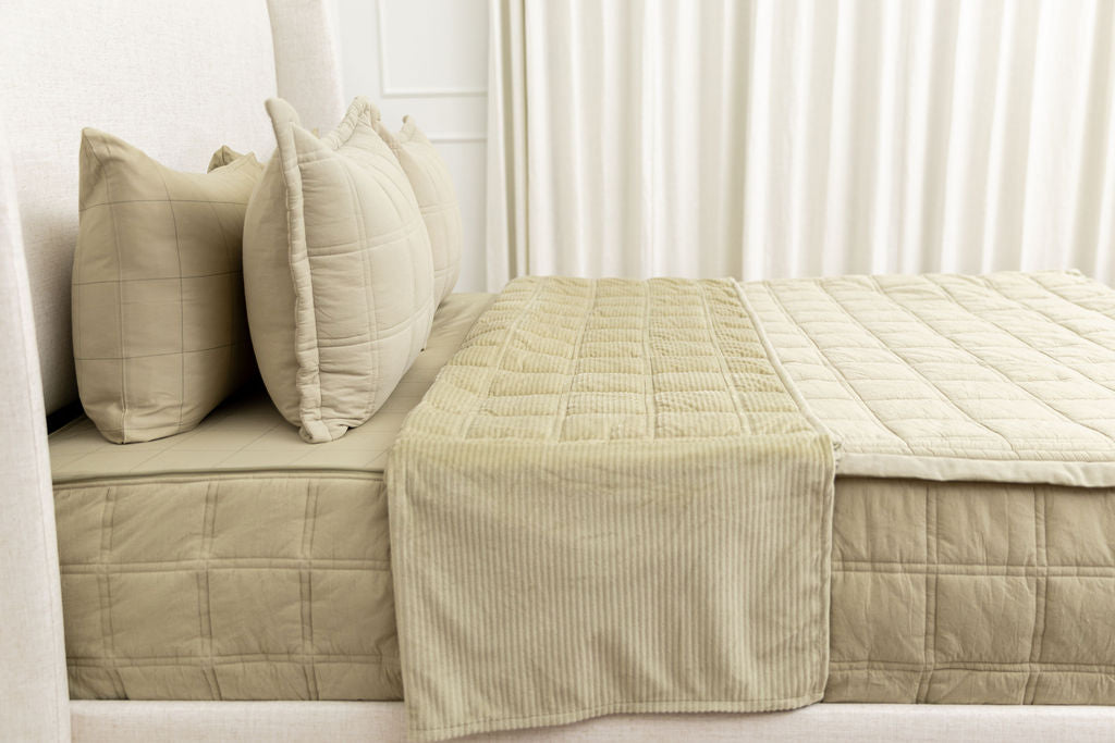 A side view of a khaki quilted zipper bedding on a bed with the top unzipped halfway down revealing the minky comfort interior. 