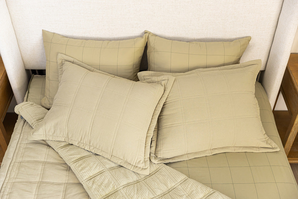 A bed made with khaki green zipper bedding, the top portion unzipped and pulled back, with four pillows arranged on top of the bed.