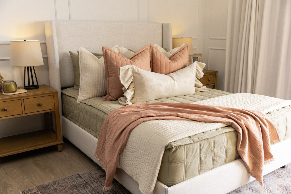 A bed made with khaki green zipper bedding and an assortment of neutral and pink pillows and blankets.