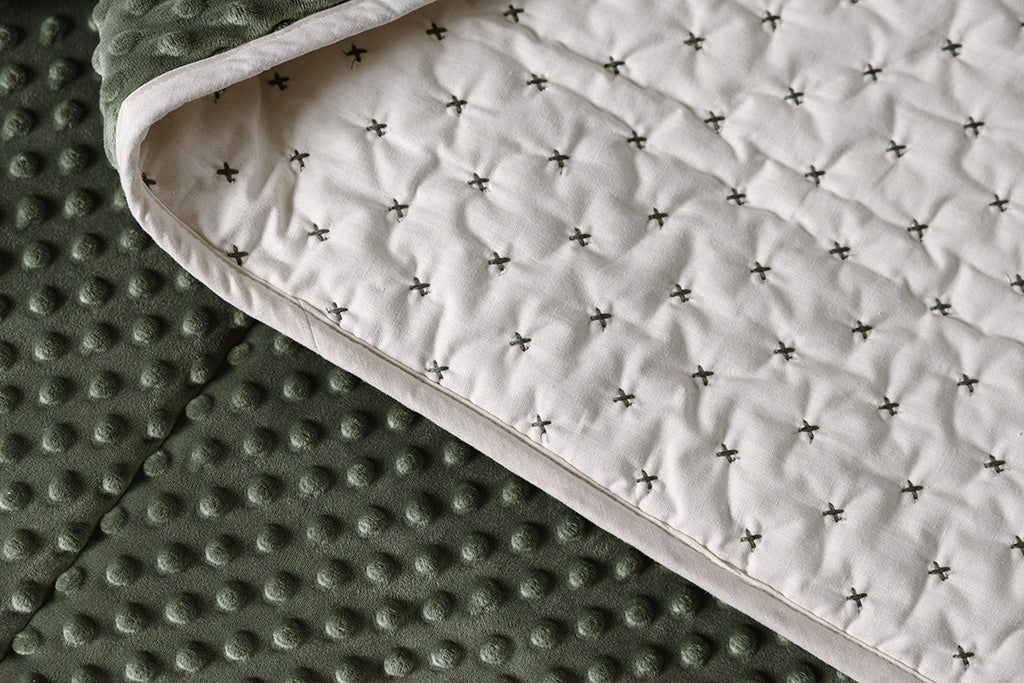 A close up of a creamy white blanket exterior with green "x" stitching and it folded over to reveal the green minky interior.