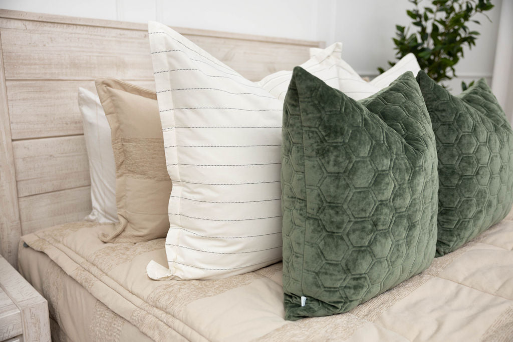 A close up view of a bed made with tan zipper bedding and neutral and velvet green pillows.