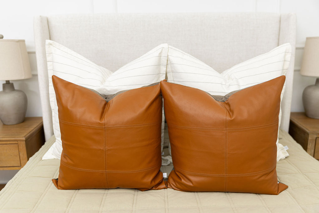 A bed made with khaki zipper bedding with an an assortment of cream striped and leather pillows.