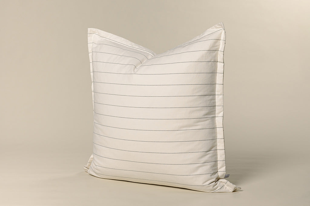 A white and grey striped pillow on a cream paper backdrop.