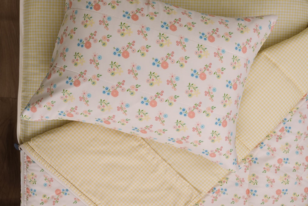 Yellow gingham and flower printed kids zipper bedding with the top unzipped and one side pulled back to reveal the inside lining, the pillow tossed on top of the bed.