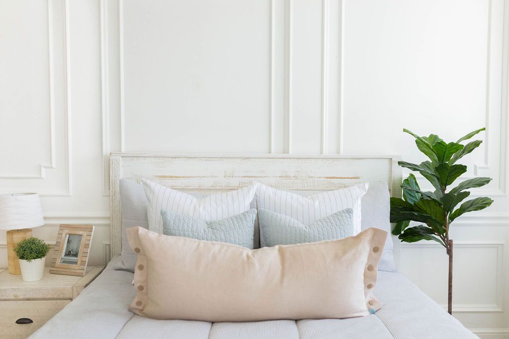 A brightly lit bedroom with a bed made with light gray waffle textured zipper bedding and an assortment of neutral pillows.