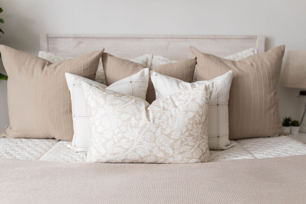 A close up view of a queen bed made with cream embroidered zipper bedding and an assortment of patterned neutral tan pillows and blanket.