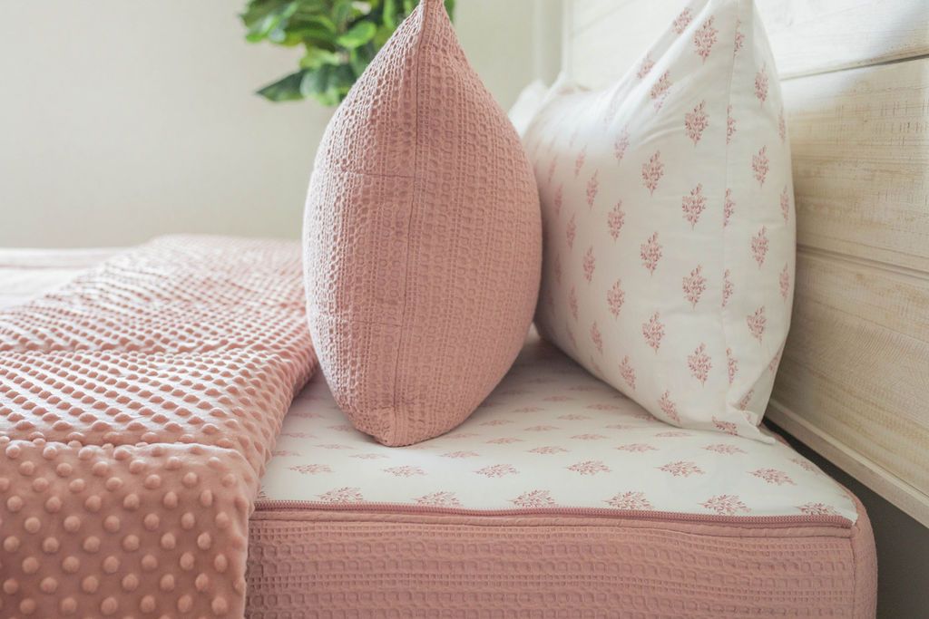 An up close side view of a bed made with pink woven zipper bedding with the top unzipped partially down the bed and the comforter folded down.