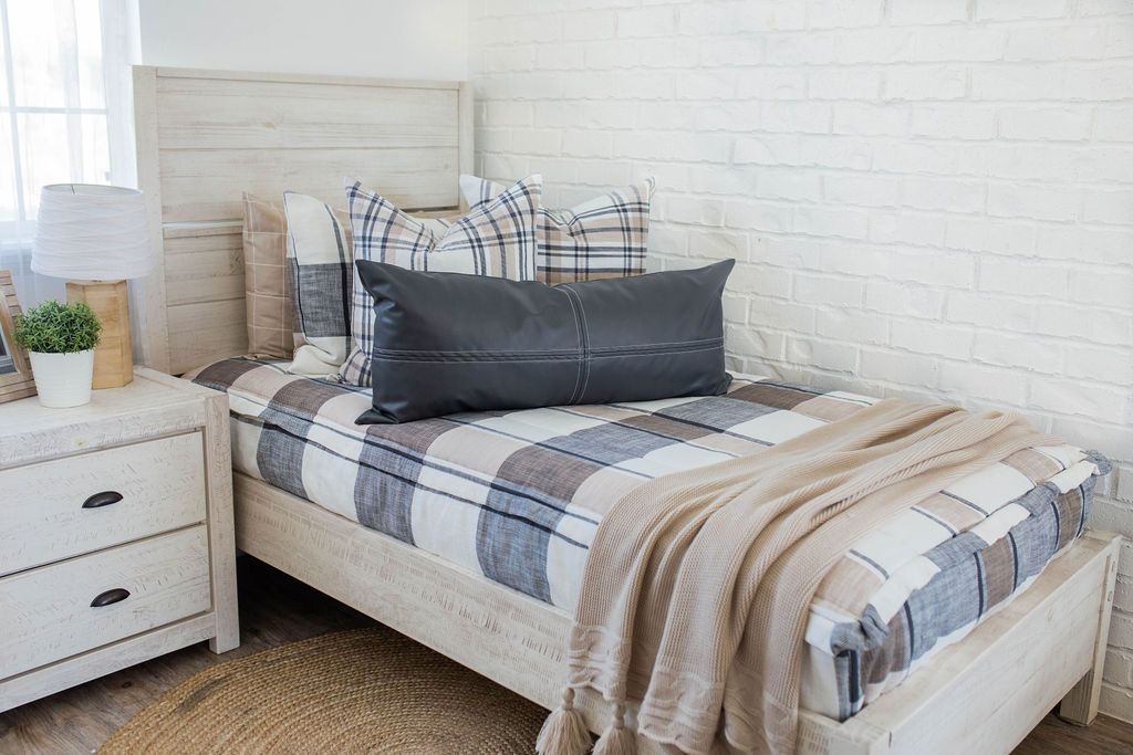 A twin bed made with white, tan, and gray plaid pattern zipper bedding with an assortment of neutral pillows and blanket.
