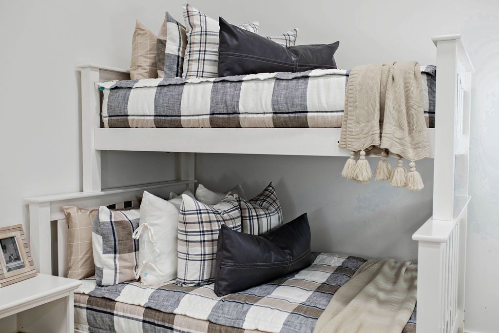 A standard bunk bed with both bunks made with cream, tan, and gray plaid pattern zipper bedding and neutral and leather pillows and blankets.