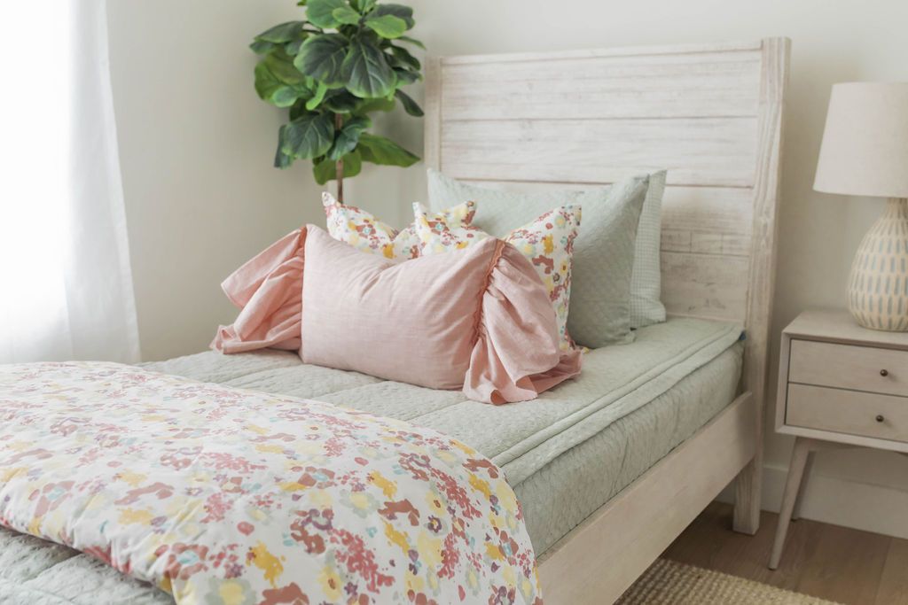 A close up view of a twin bed made with sage green zipper bedding and pink, green, floral pillows and blanket.