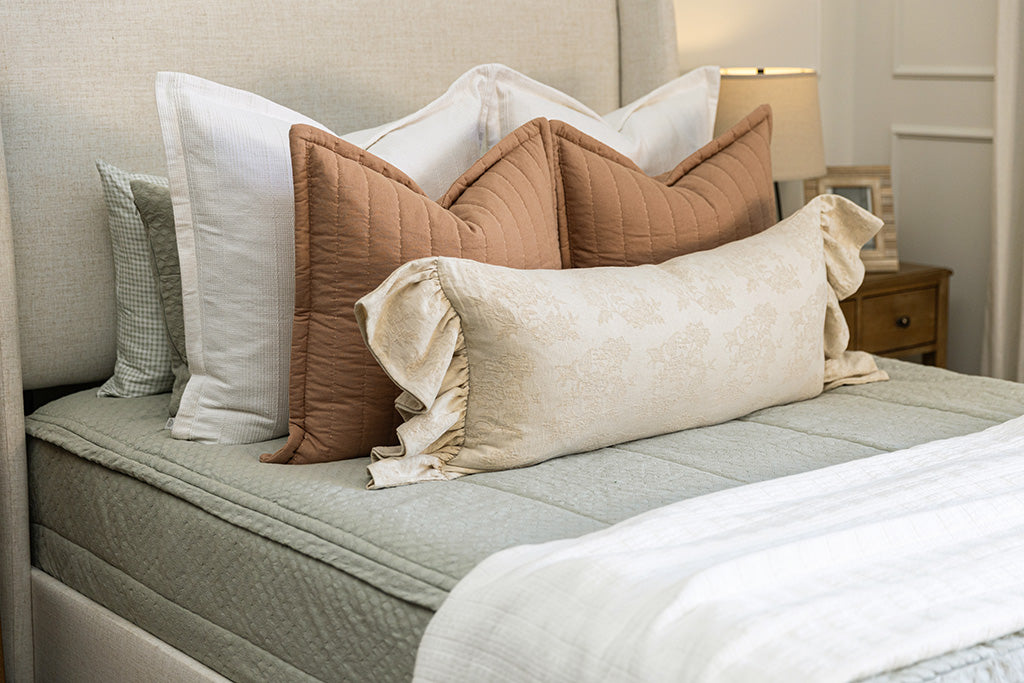 A bed made with soft green zipper bedding and an assortment of pink and multi-color floral pillows and blanket.