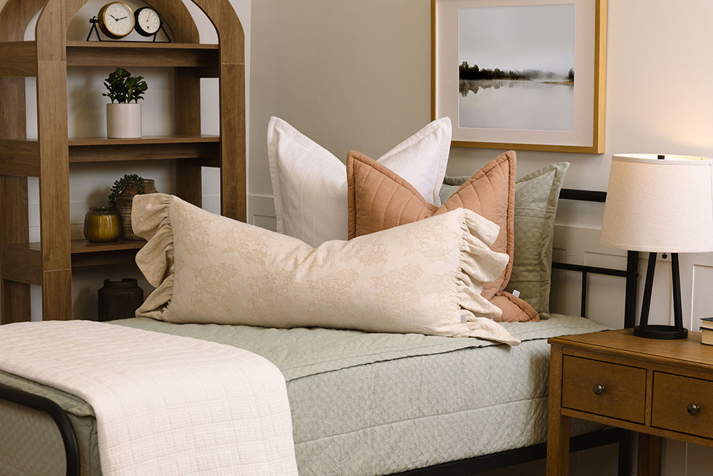 A close of view of a bed made with soft green zipper bedding and pink, white, and cream pillows and blanket.